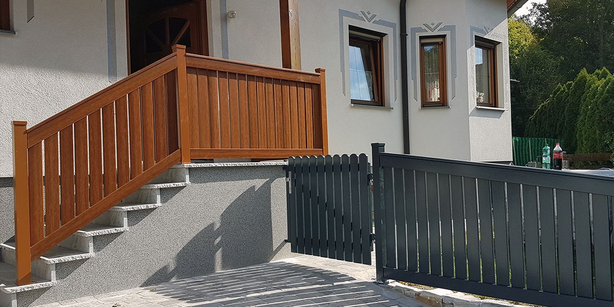 Ein Holzzaun und eine Treppe führen zu einem Haus, umgeben von einer grünen Landschaft.
