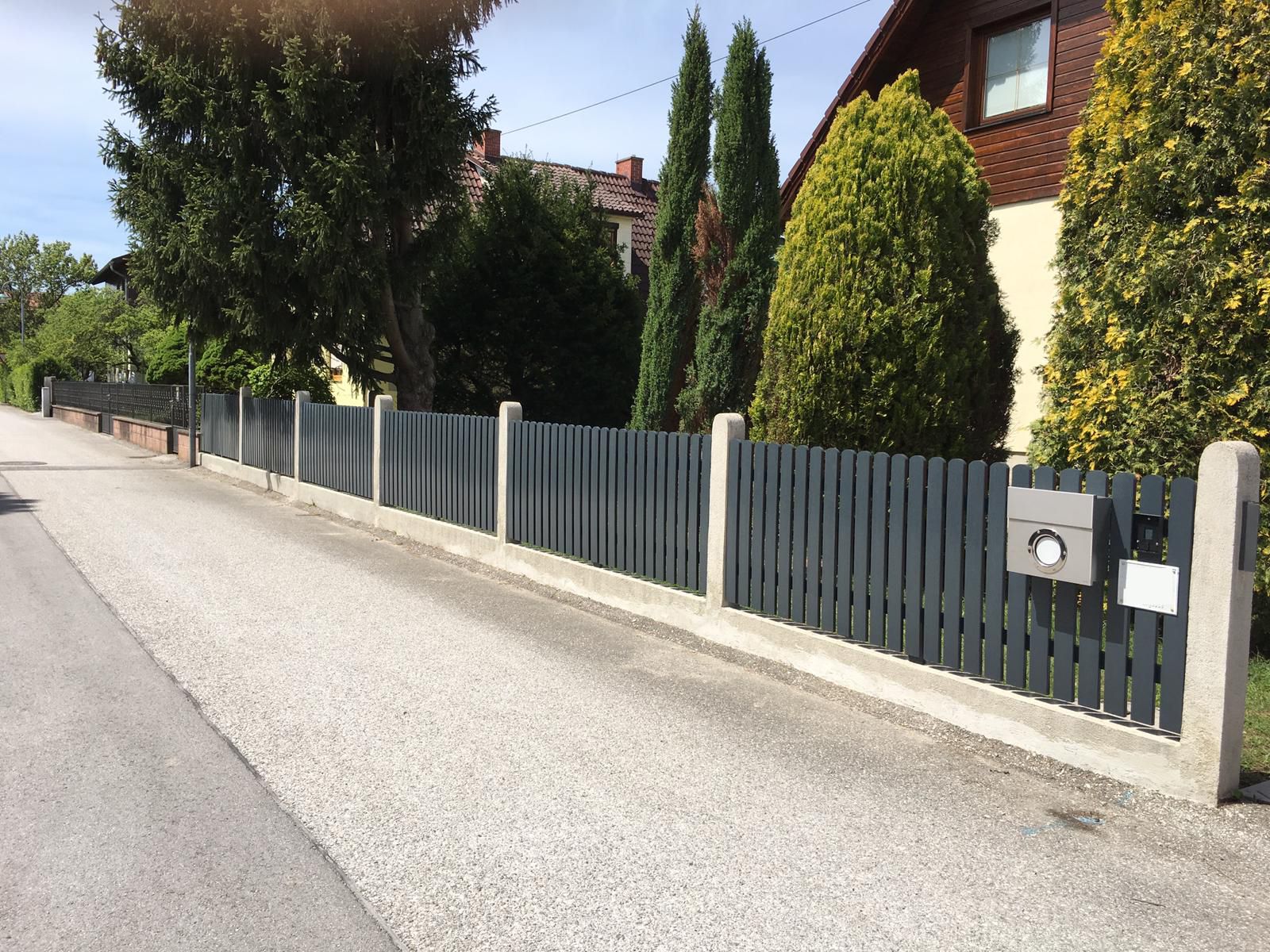 Ein Zaun steht neben einer Straße, in der Nähe befindet sich ein Briefkasten.